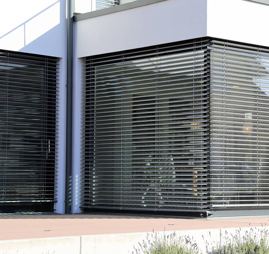 Eine Außenansicht eines Gebäudes mit heruntergelassenen, silbernen Außenjalousien