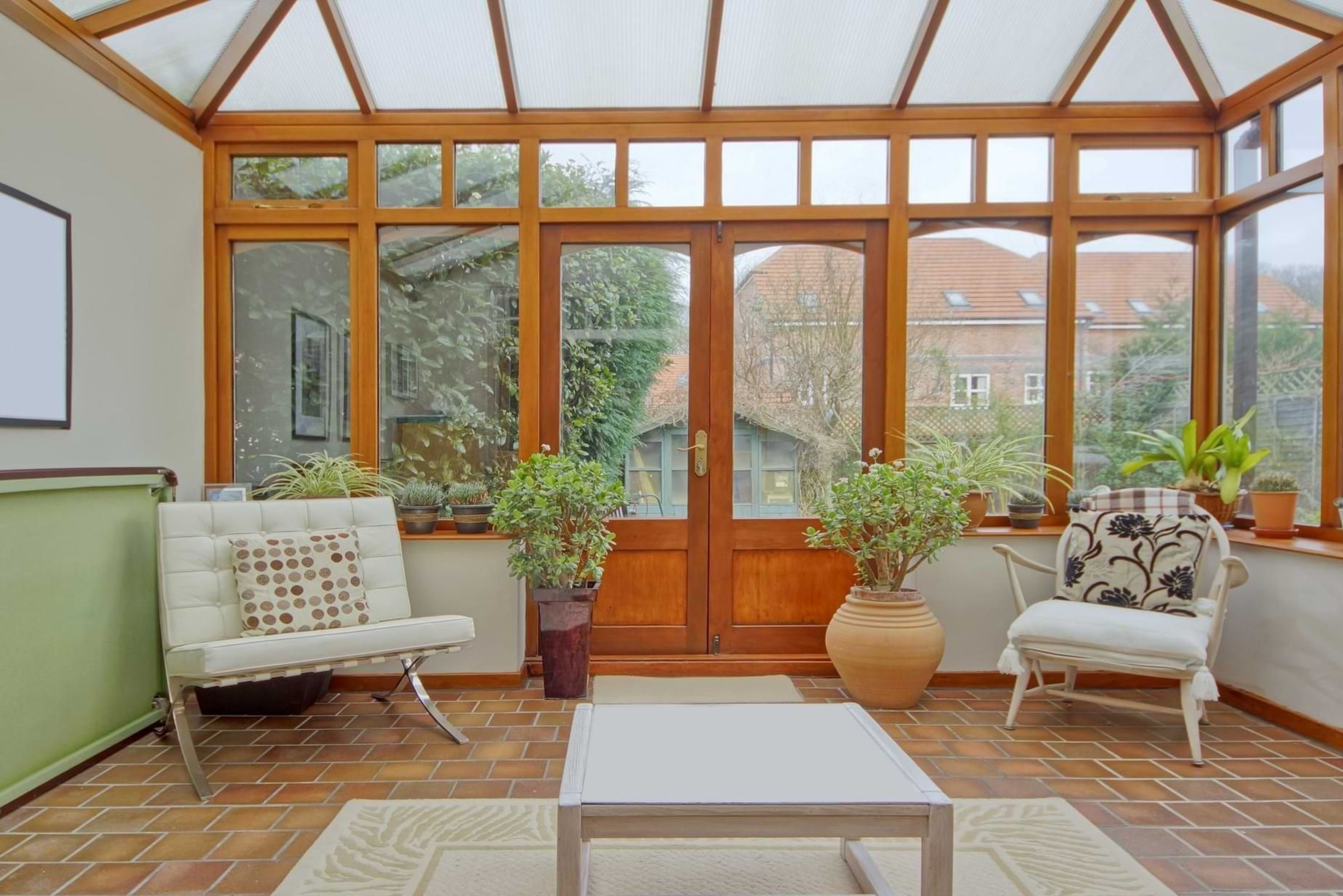 Ein lichtdurchfluteter Raum mit Holztüren, einer Fensterbank voller Pflanzen und einer Sitzgelegenheit mit stilvollem Polsterbezug
